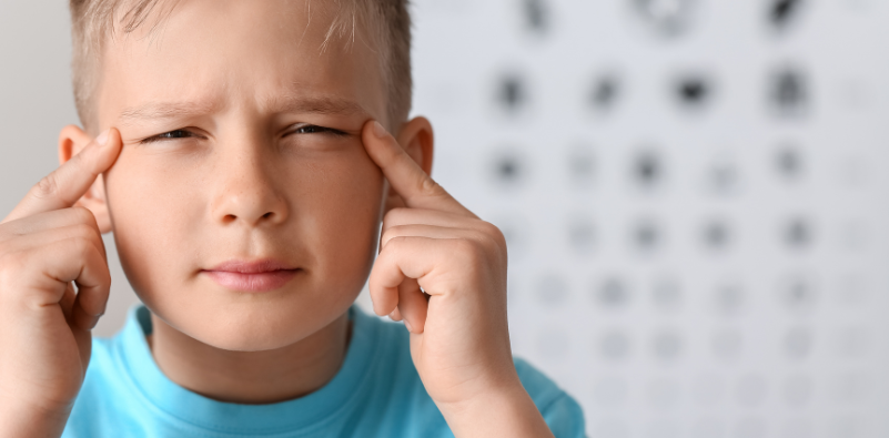 A child squinting, with his fingers on his temples.