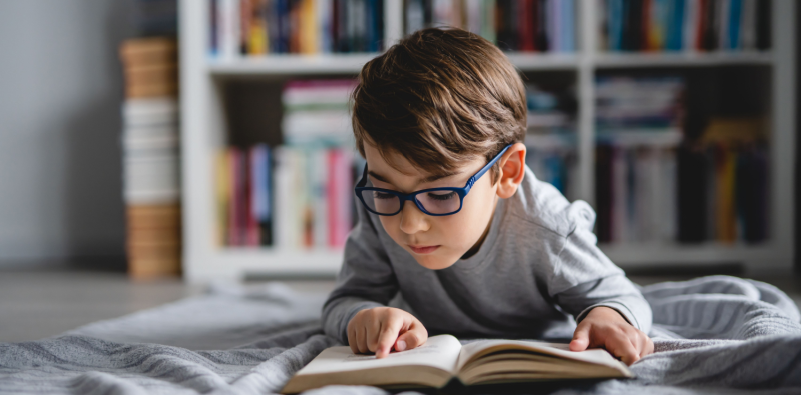 Child reading at close distance showing myopia risk factors and vision care importance.]