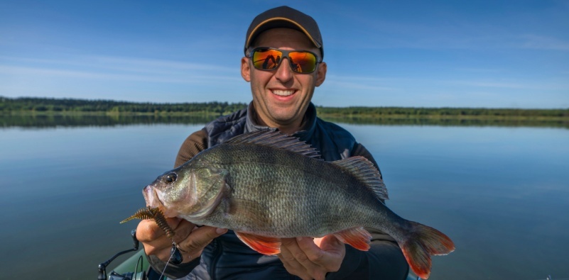 A fisherman holding a fish, wearing polarised sunglasses.