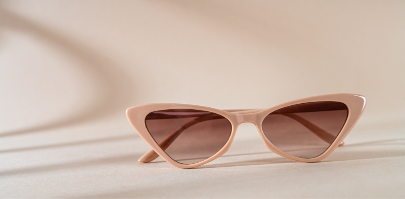 A pair of peach-coloured cat-eye sunglasses in a neutral space.