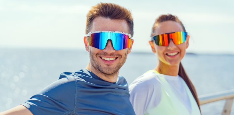 Couple wearing colourful sports sunglasses by the sea