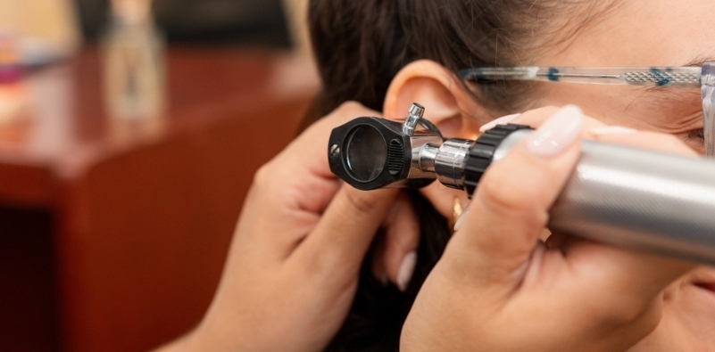 An audiologist looking into a patient’s ear with an otoscope during consultation