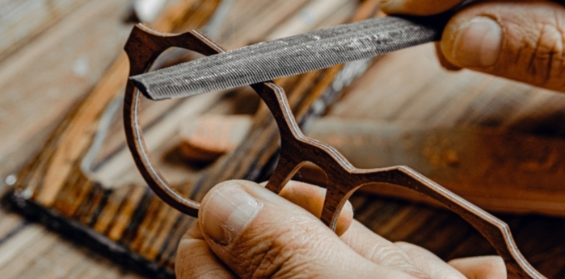 A wooden glasses frame being filed down to shape by hand
