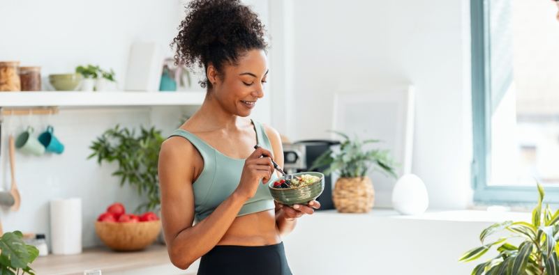 Athletic woman eating a healthy fruit bowl in the kitchen at home