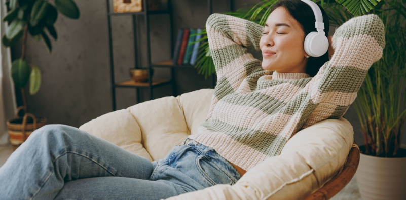 Woman in casual clothes listening to music in headphones sat in an armchair