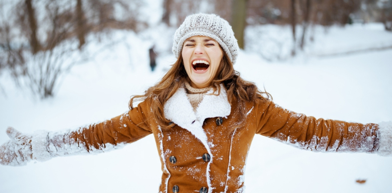 Smiling stylish woman in brown hat and sheepskin coat outside in the snow