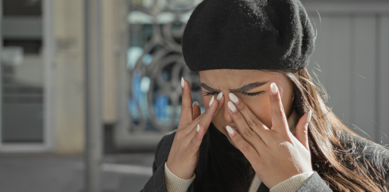 A young woman wearing a black beret, rubbing her eyes in the street