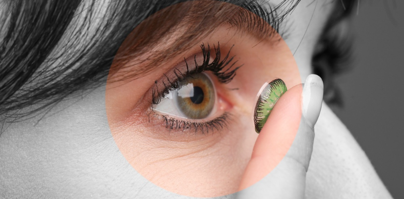 Young woman putting in green contact lens, closeup. Black and white toning with the eye and contact lens in colour